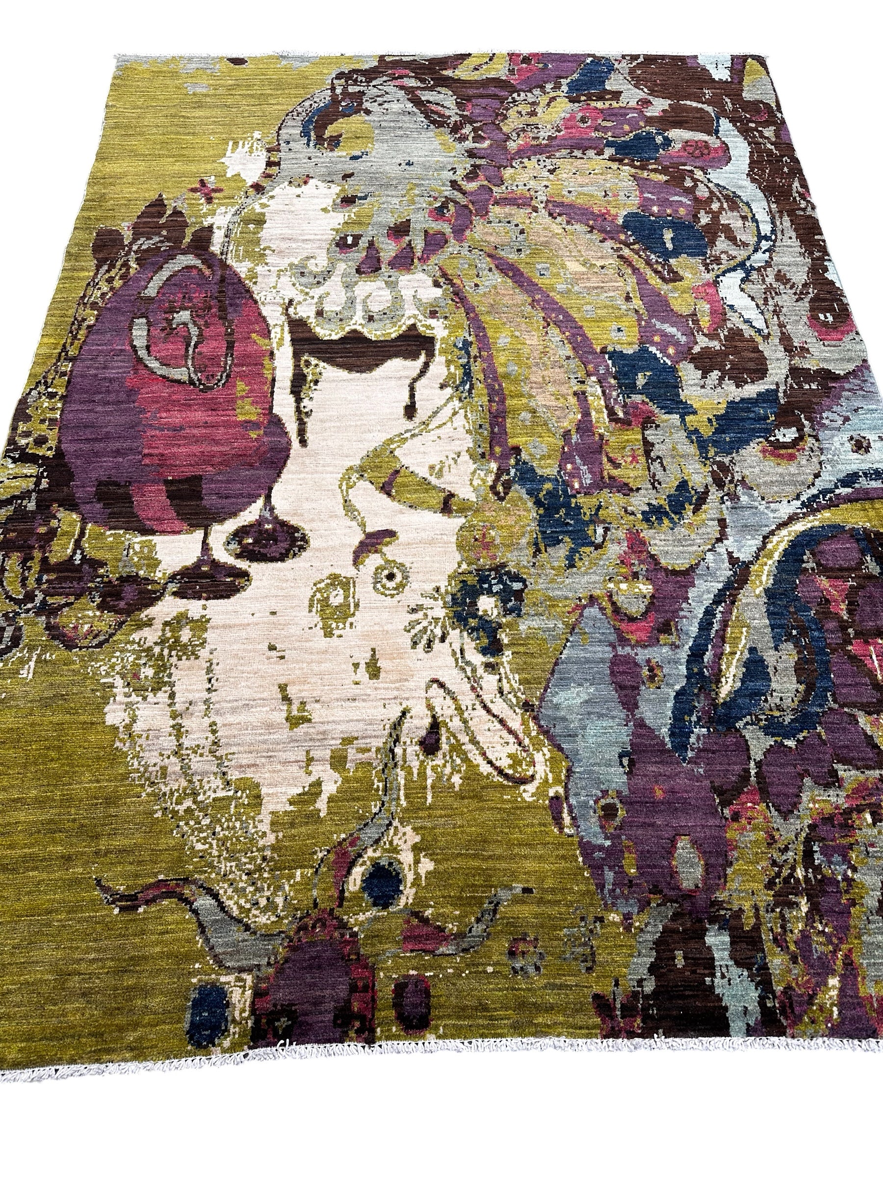 An abstract area rug with a distressed, painterly design featuring a stylized face in purple, cream, gold, and blue tones.