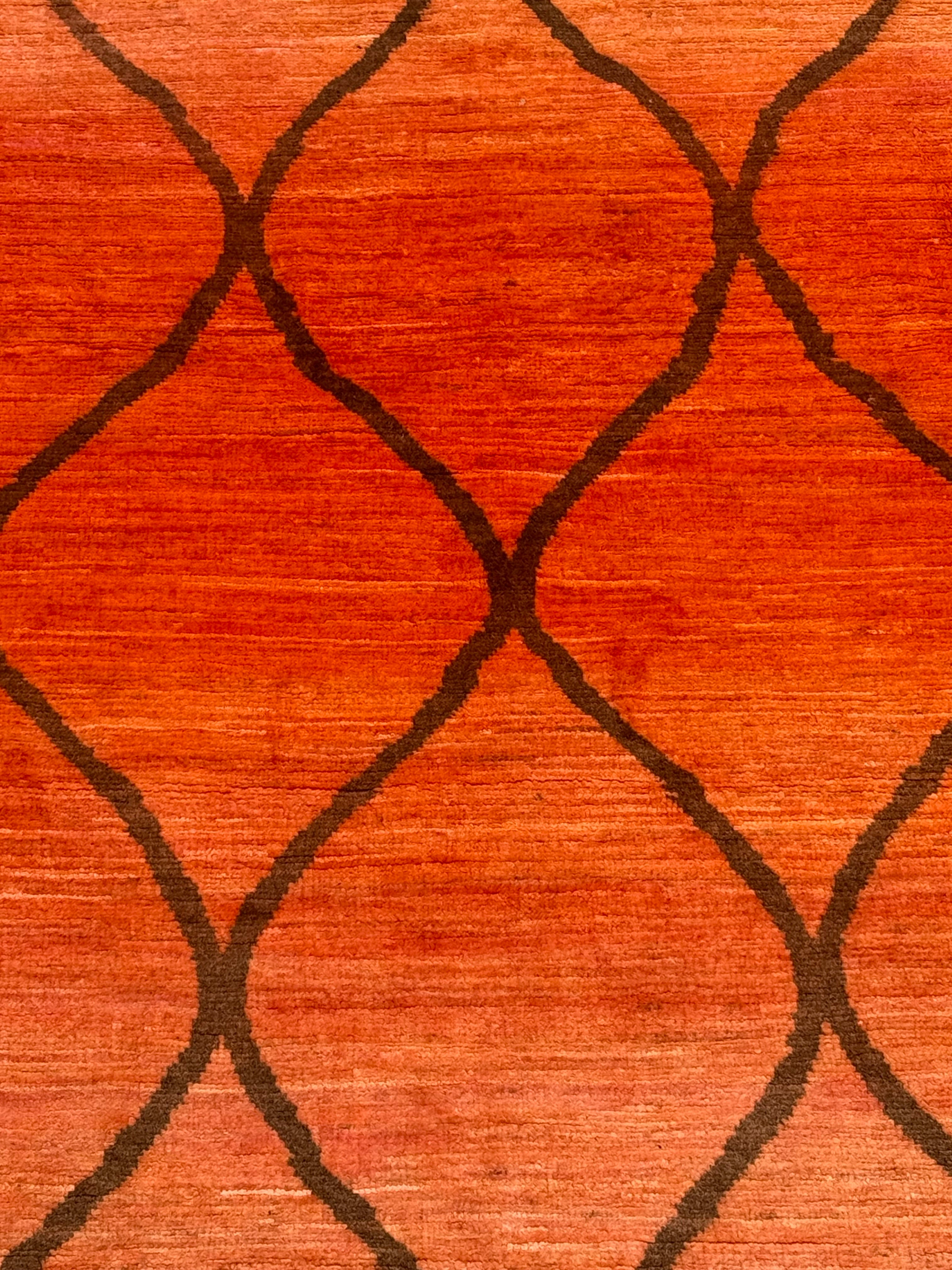 A close-up of a textured orange-red rug with a dark brown geometric pattern.